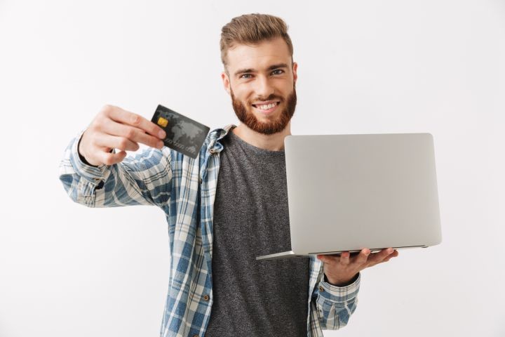 右手にクレジットカード、左手にノートパソコンを持っている男性の画像
