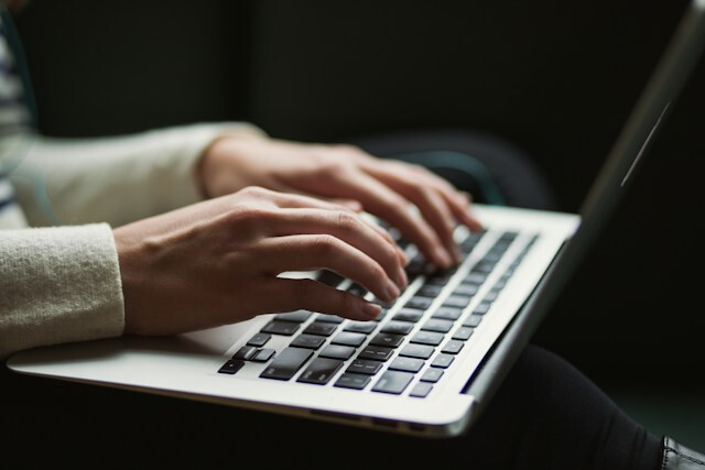 膝の上でノートパソコンを操作する男性の手元