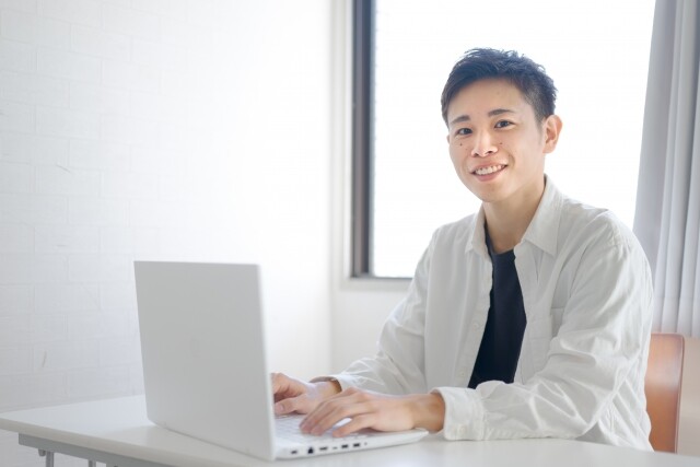 パソコンで仕事をしながら微笑む男性