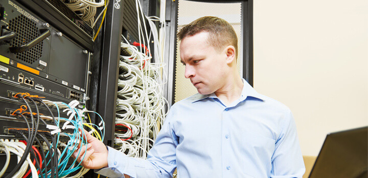 たくさんのケーブルが繋がれている大きなコンピュータを前に真剣な表情で作業している男性の画像